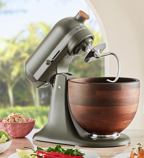 An image of the Kitchen Aid Design Series Stand Mixer with dough hook attachment installed. The bowl has a wooden look while the machine has a dark green finish,