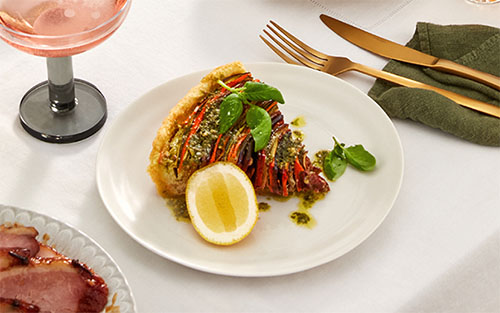 A plate with a slice of a vegetable tart, garnished with a lemon wedge and herbs.