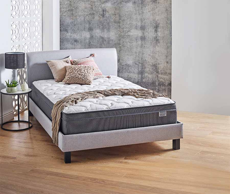 SleepMaker® Dakota Deluxe Queen Mattress with a throw and cushions on it.