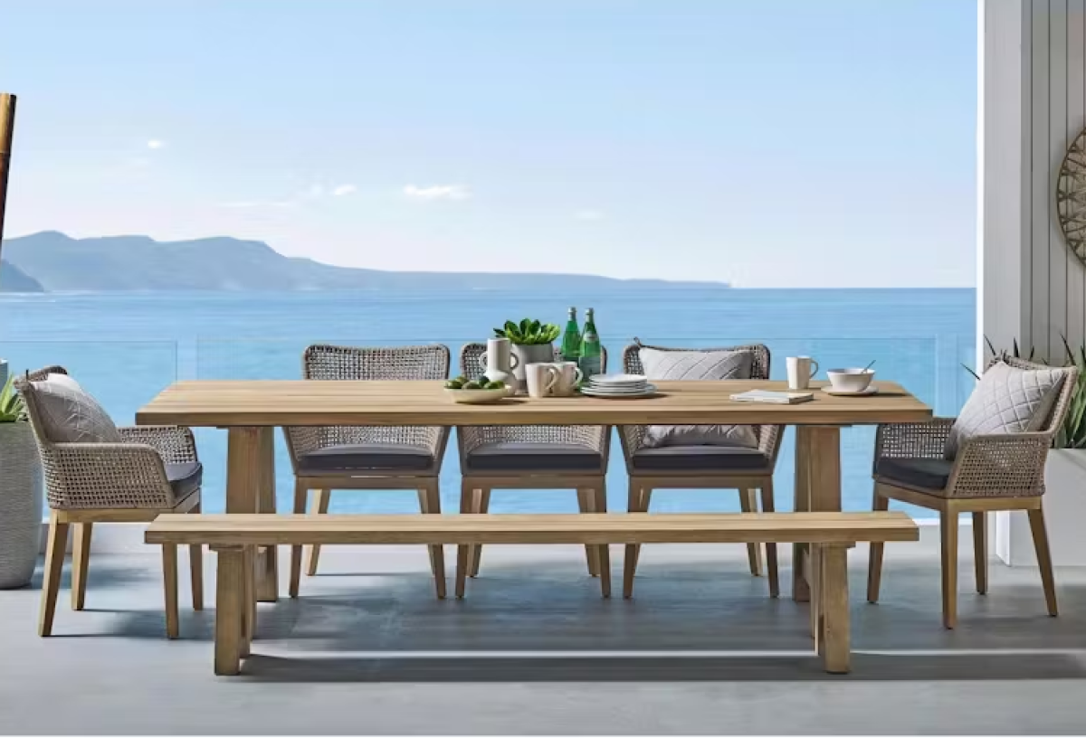 Harvey Norman exclusive Panama eucalyptus outdoor dining table with woven chairs and timber bench overlooking the ocean. 