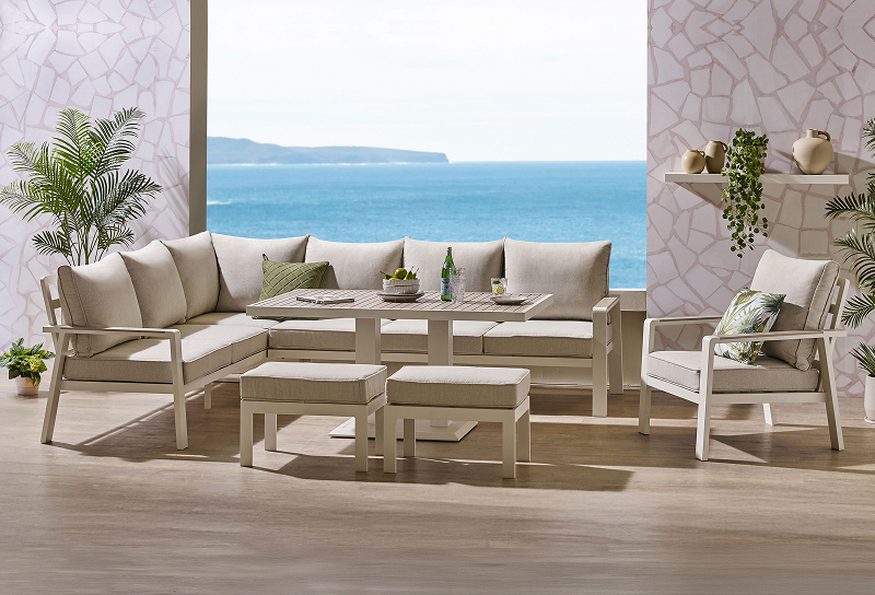 Coastal outdoor lounge setting with cream sofa, armchairs, ottomans and coffee tables overlooking the ocean. 