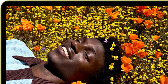 MacBook Neo, citrus colour, screen shows a smiling person lying in a sunny field of flowers