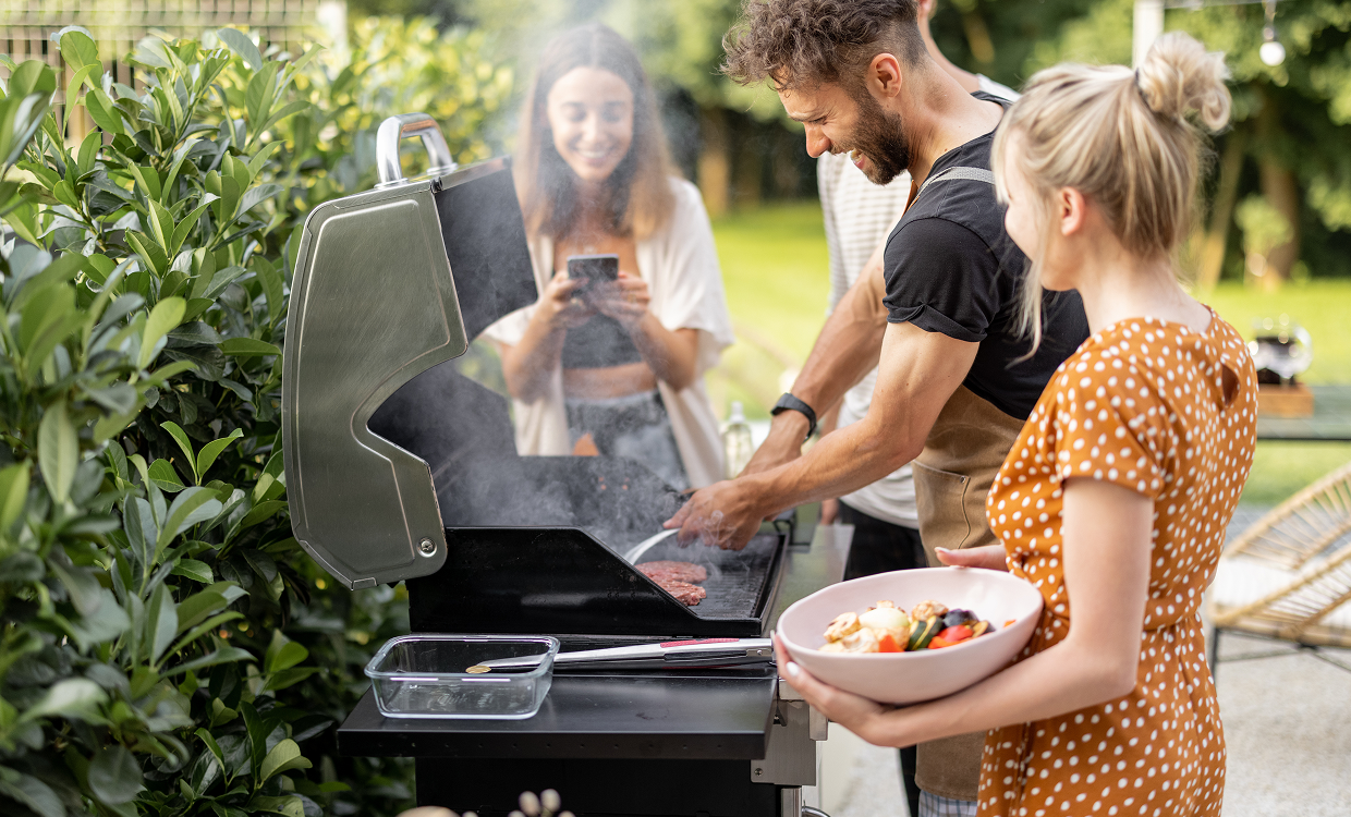 Friends cooking burgers and vegetables on a BBQ in a sunny backyard